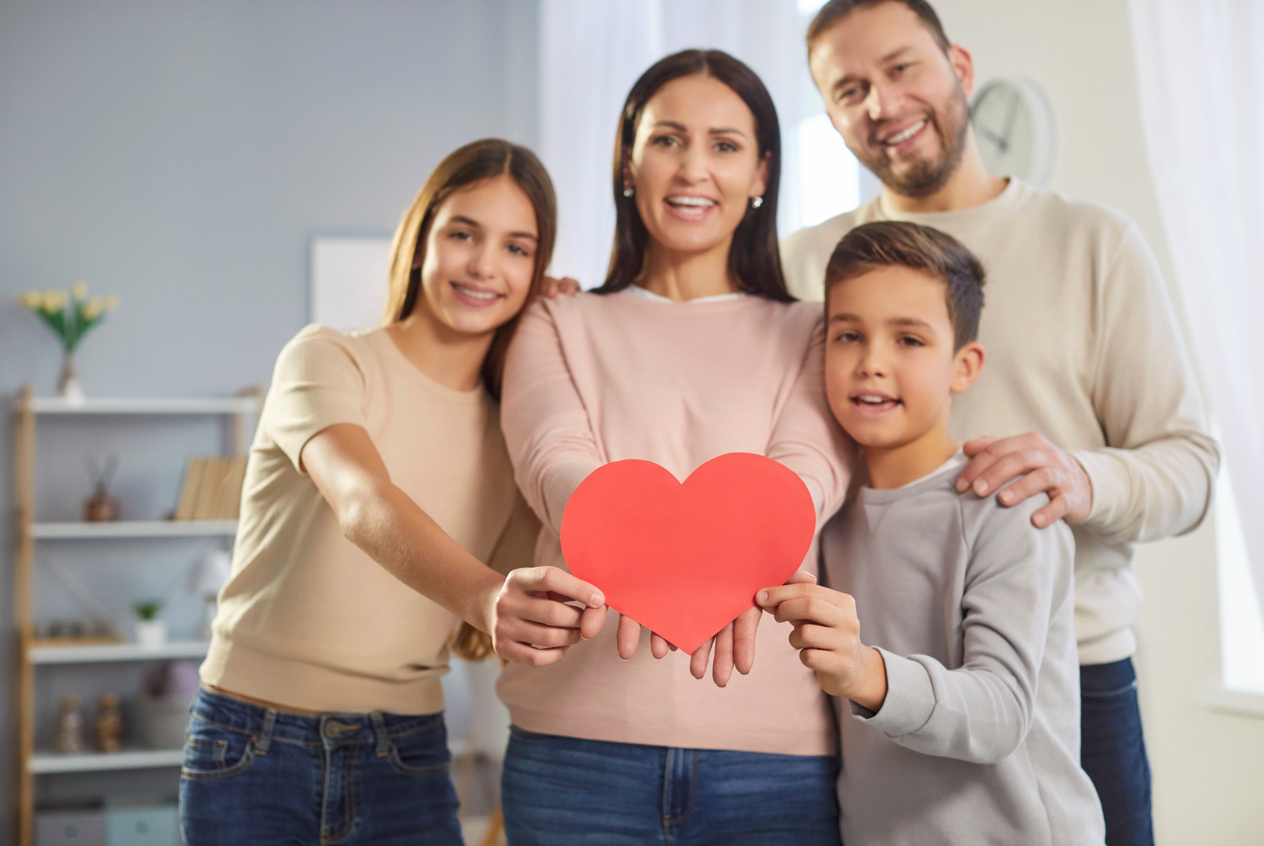 Happy mother father and two children posing together showing big heart postcard celebrating Valentines Day in family circle, have good relationships express love to everyone, posing over home interior