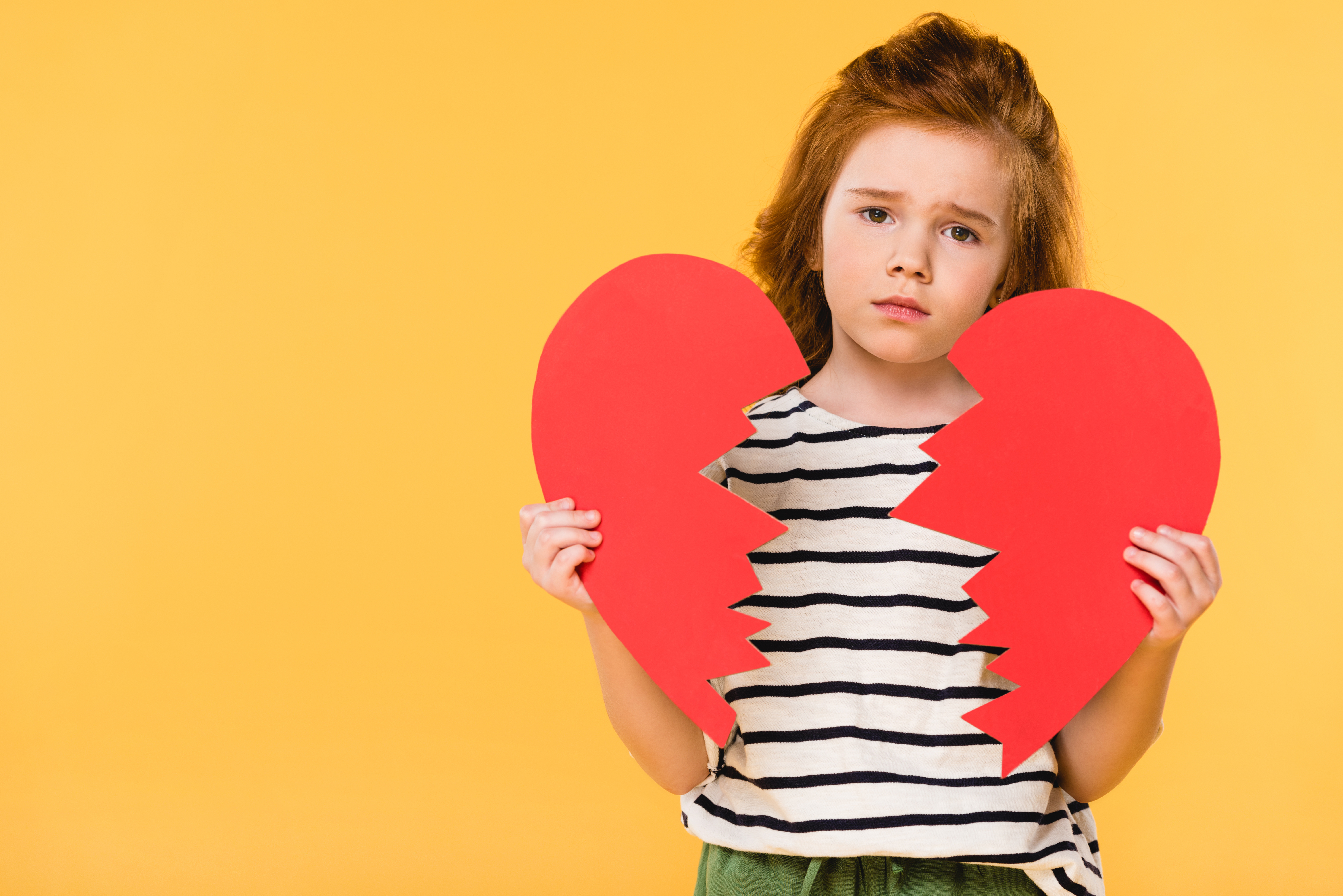 portrait of sad child with broken red paper heart isolated on yellow, st valentines day concept