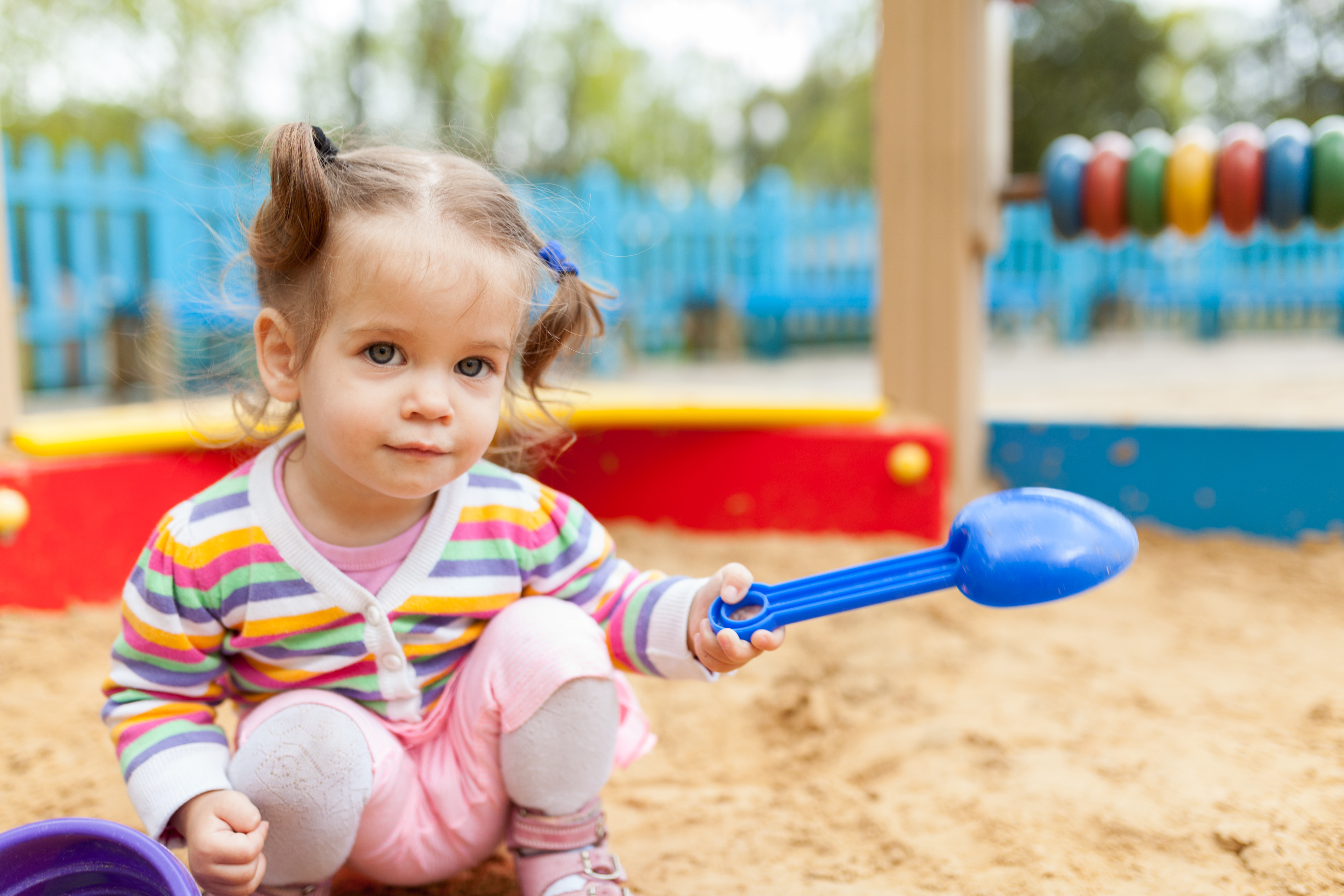 a little girl with two tails is dressed in a striped colorful jacket is playing in the sandbox on the playground Summer family leisure concept