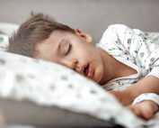 Little blond boy sleeping in his bed. Restless sleep of a baby with a cold. The kid sleeps with his mouth open. My little boy sleeping by the light of the window.