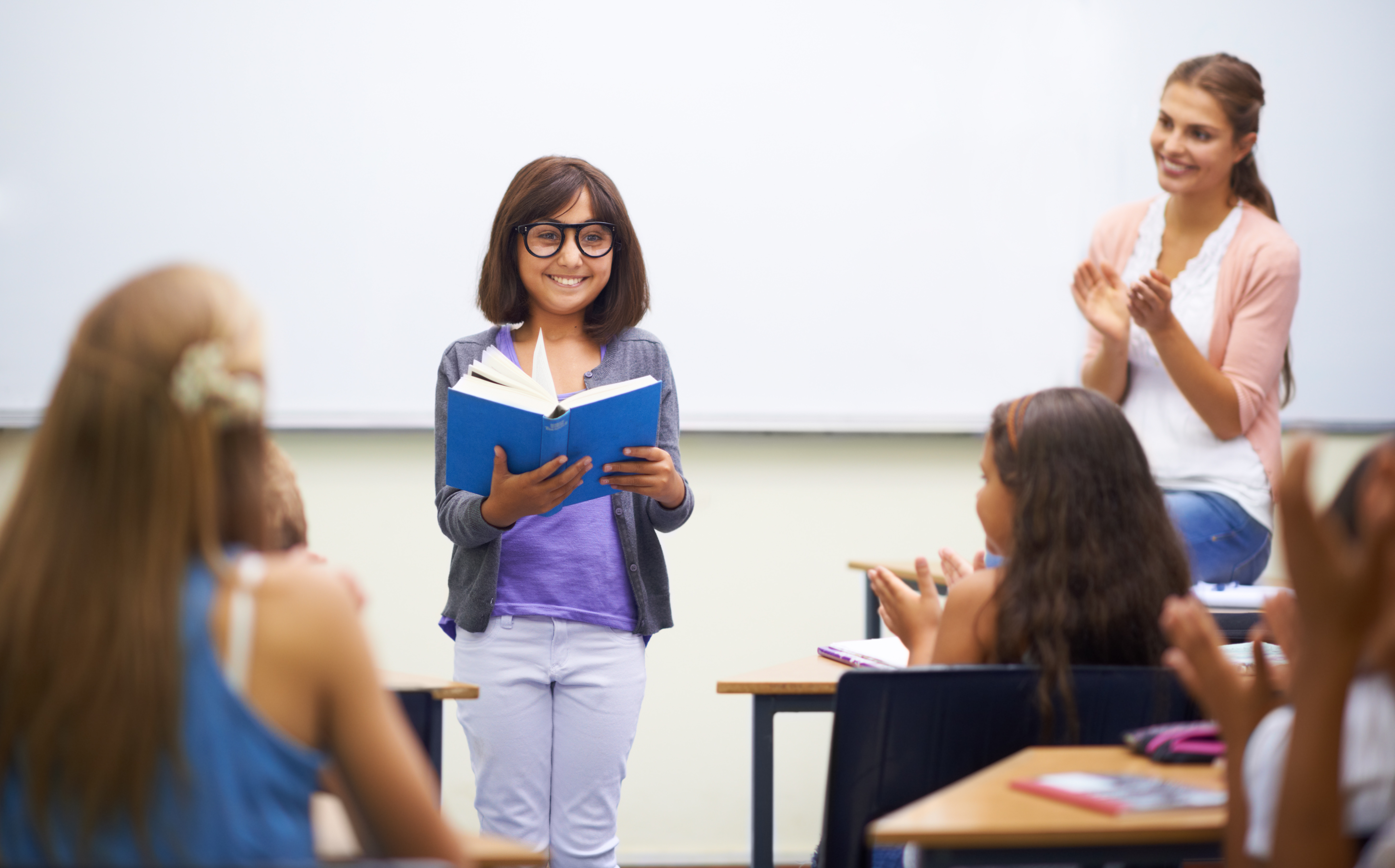 A young girl doing prepared reading at the front of the class.