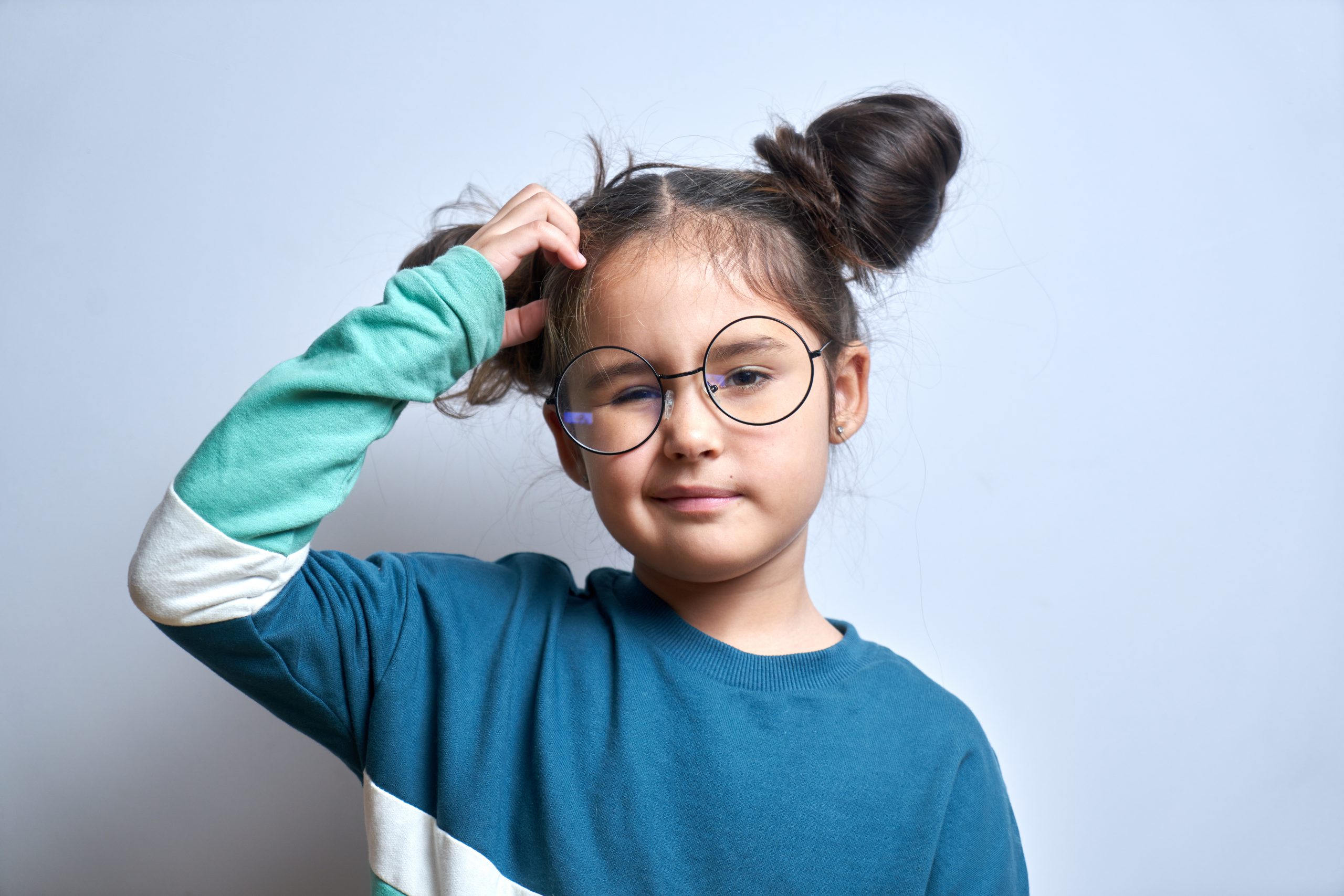 Funny little girl in glasses scratching her head doubts, makes decision isolated on yellow studio background