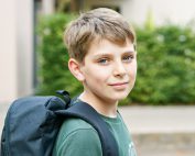 Happy preteen kid boy with backpack or satchel. Schoolkid in on the way to elementary or middle school on warm sunny summer day. Healthy child outdoors on the street in the city .
